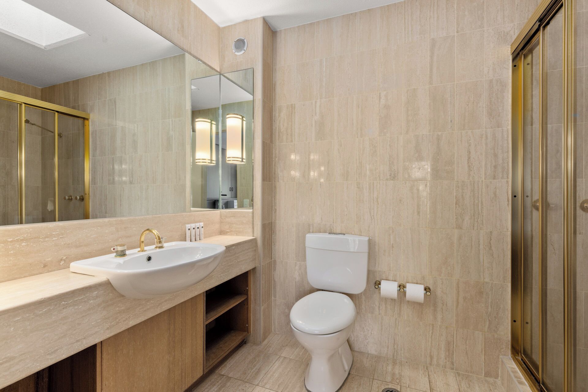 A modern bathroom with a large mirror, a sink with a gold faucet, a toilet, and a shower area.
