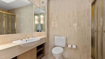 A modern bathroom with a large mirror, a sink with a gold faucet, a toilet, and a shower area.