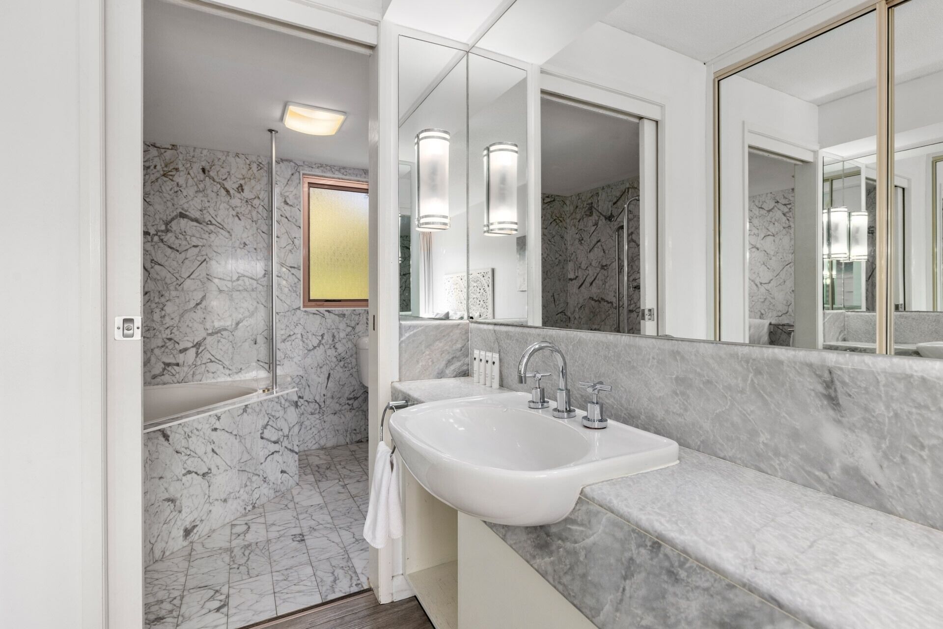 A modern bathroom with a marble sink, a large mirror, and a shower area.