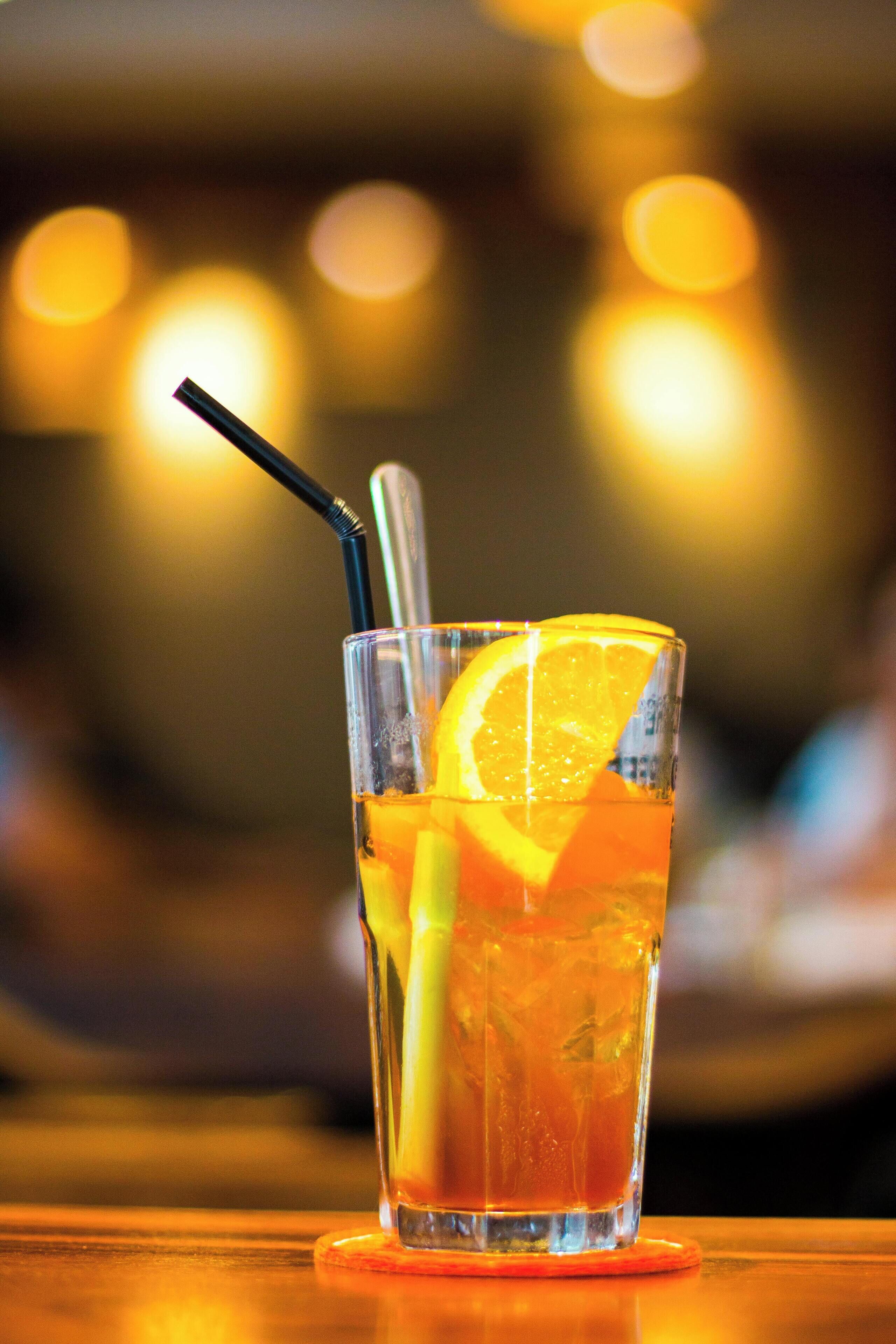 A glass of orange juice with a straw and a slice of orange on a coaster.