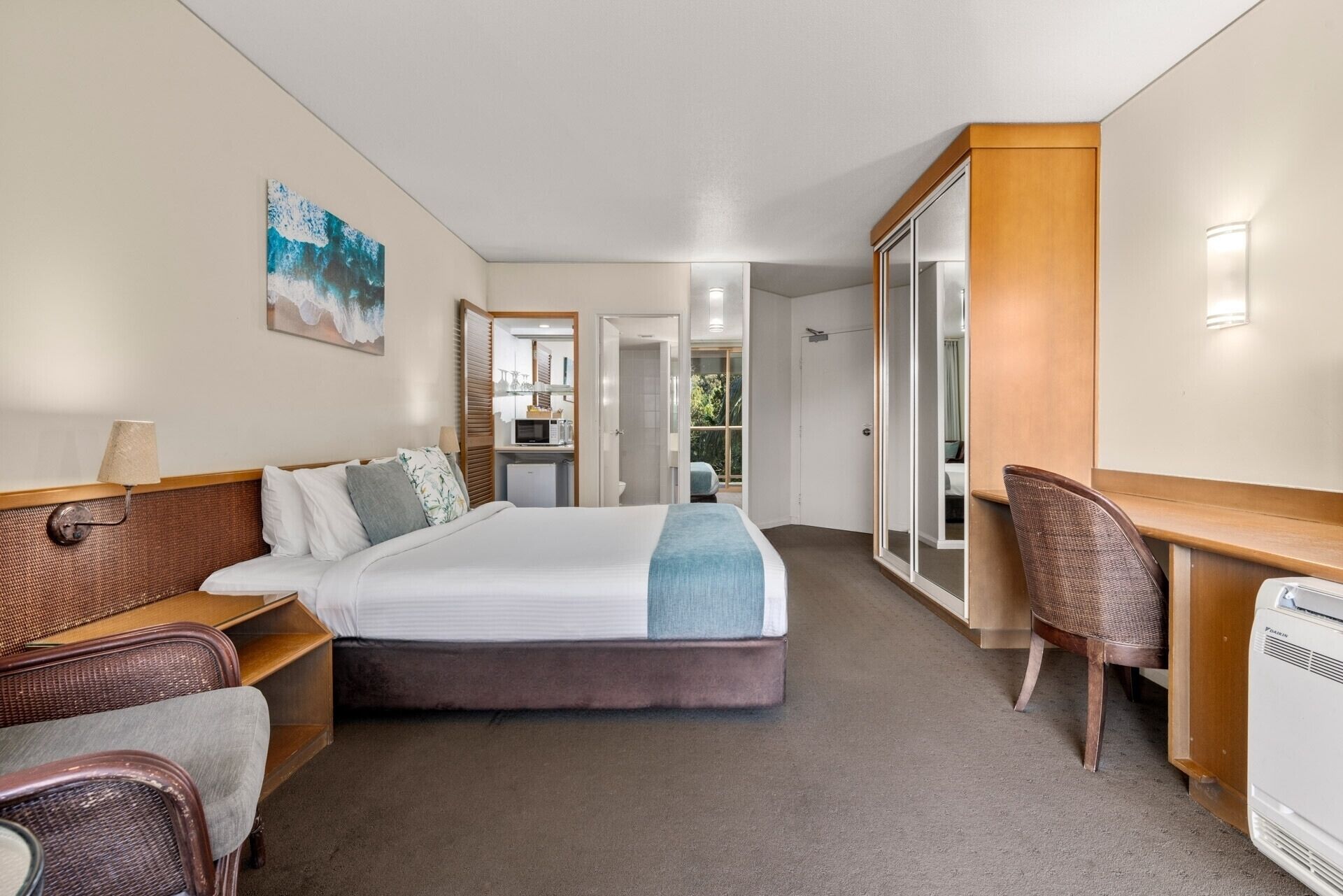Une chambre d’hôtel avec un lit, un bureau, une chaise, une armoire et une salle de bain visible à travers une porte ouverte.