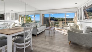 Un vaste espace de vie doté d’une grande fenêtre offrant une vue panoramique, un coin repas avec une table en bois et un espace détente aménagé avec des canapés et des fauteuils.