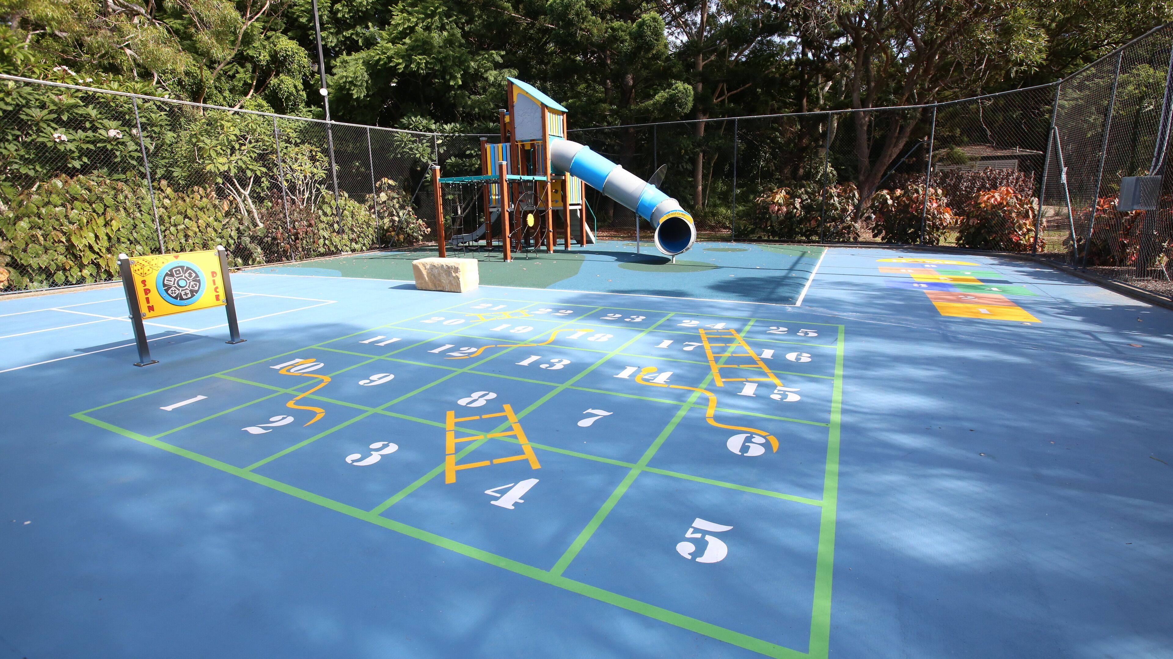 Un parque infantil con tobogán, estructura para escalar y juego de rayuela.