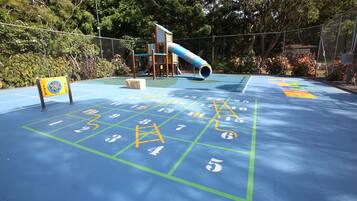 Un parque infantil con tobogán, estructura para escalar y juego de rayuela.