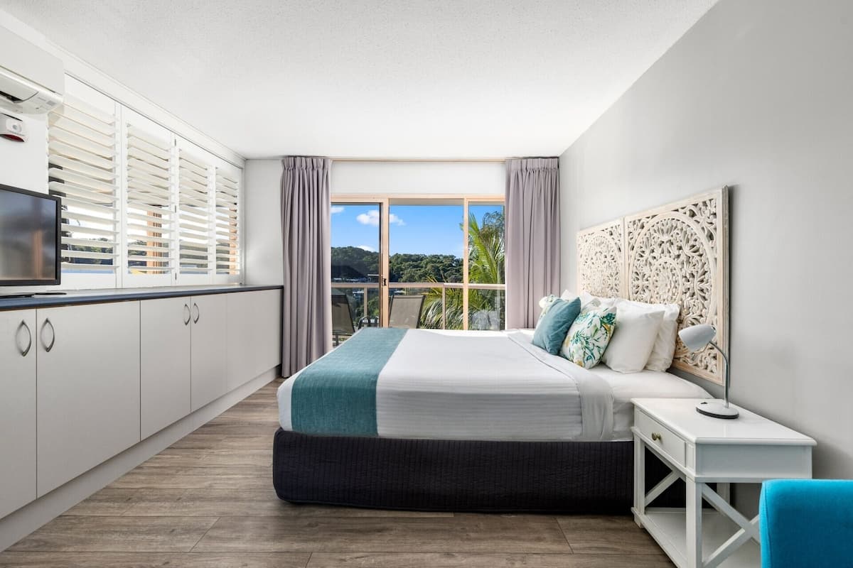 Une chambre moderne avec un grand lit, une télévision et un balcon offrant une vue sur la verdure.