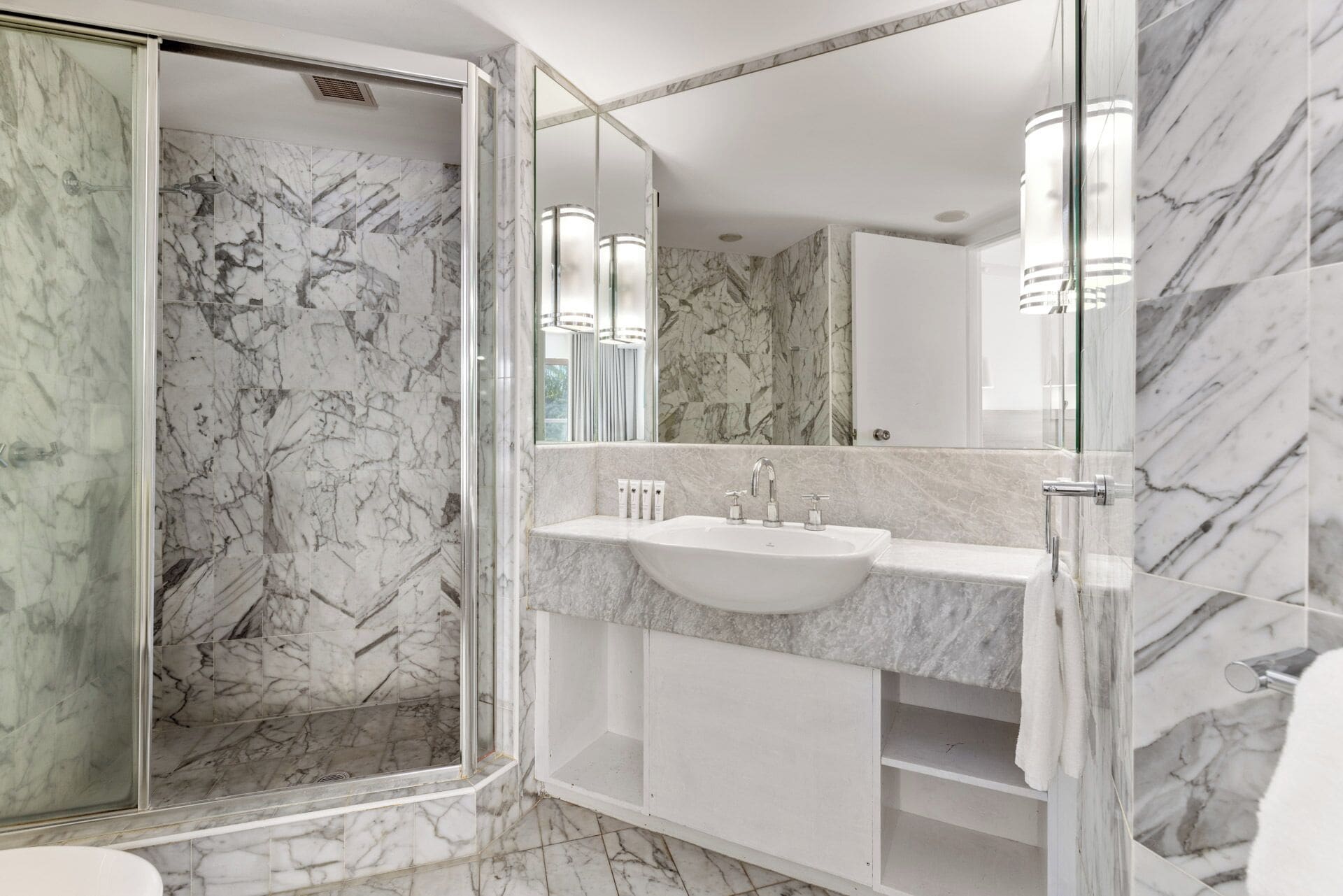 Une salle de bain moderne avec une douche à parois de verre, des murs en marbre et un grand miroir.