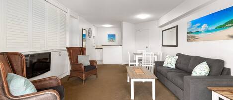 A living room with a grey sofa, wicker chairs, a wooden coffee table, a TV, and a dining area with a white table and chairs.