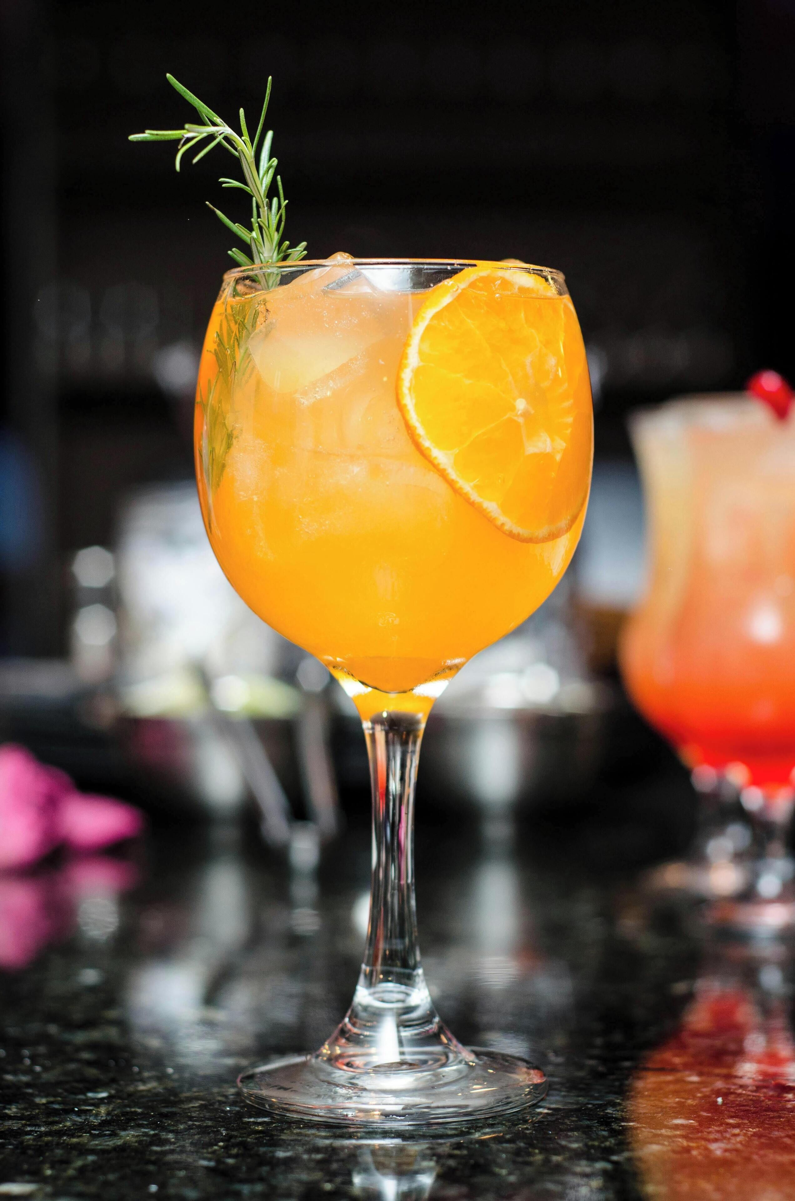 A cocktail glass with a slice of orange and a sprig of rosemary.