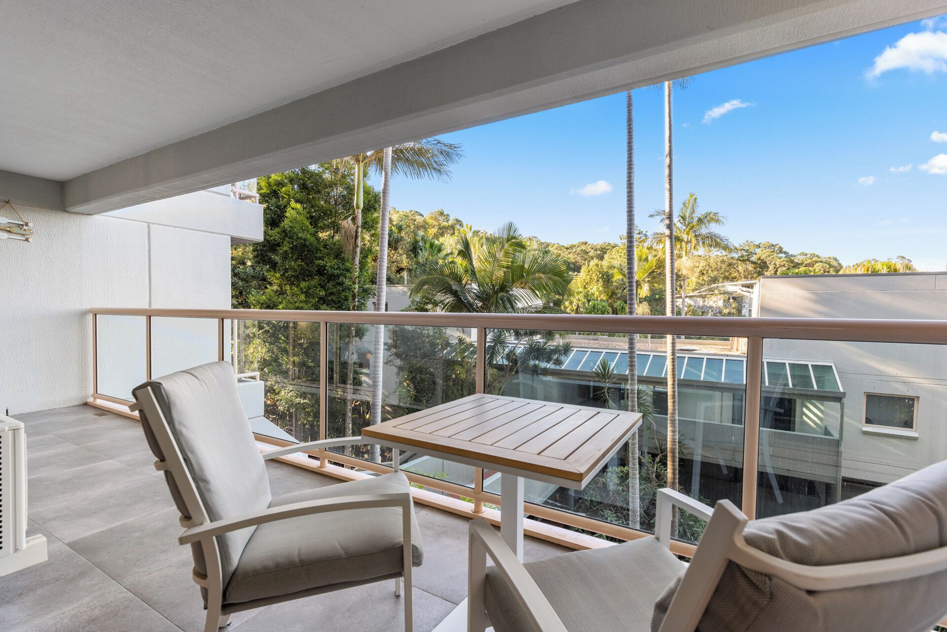 A balcony with a table and two chairs, overlooking a lush green landscape and buildings.