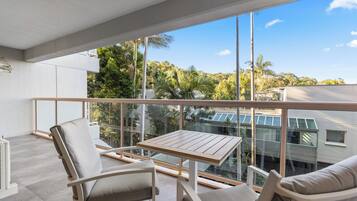 A balcony with a table and two chairs, overlooking a lush green landscape and buildings.