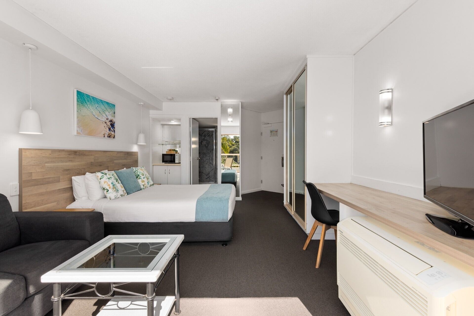 Et moderne hotelværelse med seng, skrivebord, fjernsyn, sofa og et lille tekøkken.
