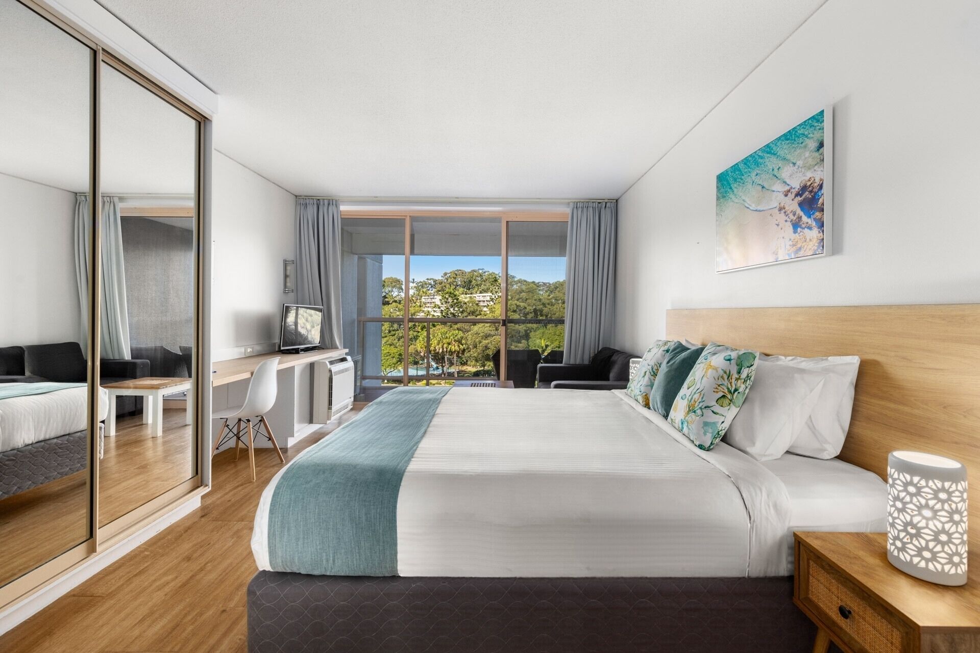 Habitación de hotel moderna con una cama grande, un escritorio, un televisor y vistas al exterior.