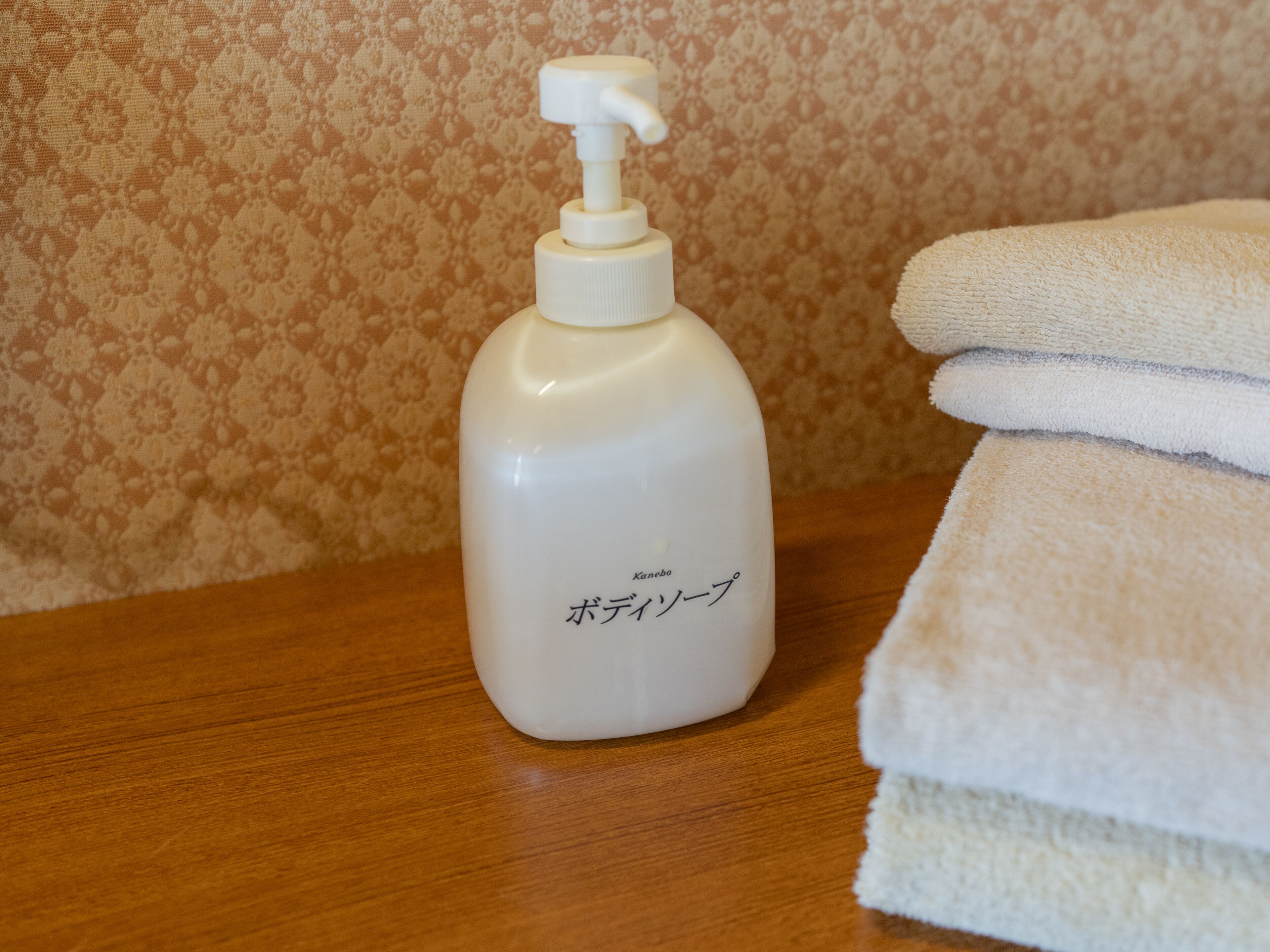 A bottle of lotion and a stack of towels on a wooden surface.