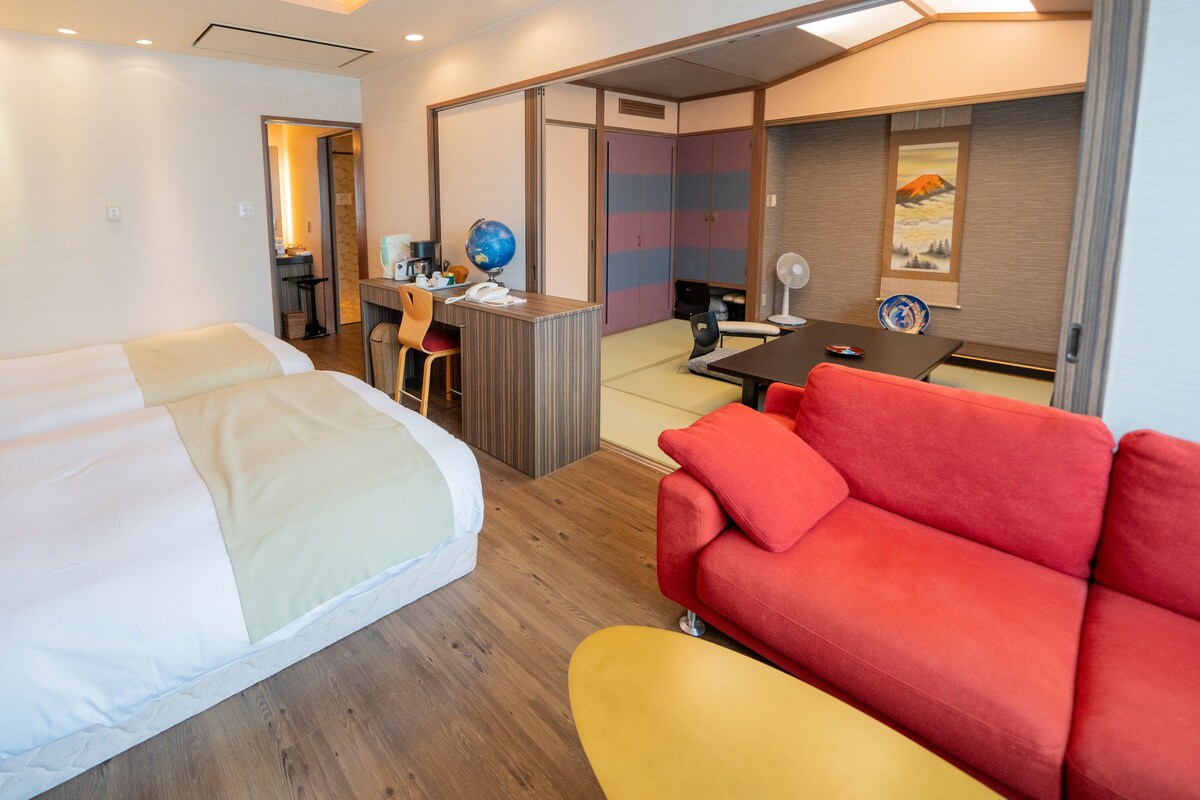 A hotel room with a bed, a desk with a globe, a red sofa, and a dining table.