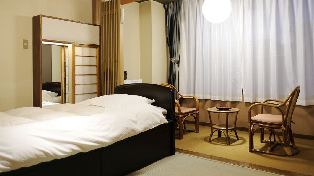 A hotel room with a bed, a mirror, a small table with chairs, and a window with curtains.