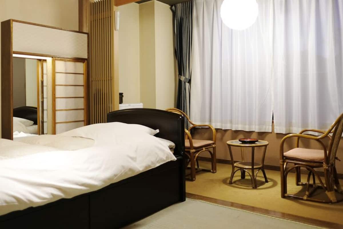 A hotel room with a bed, a mirror, a small table with chairs, and a window with curtains.