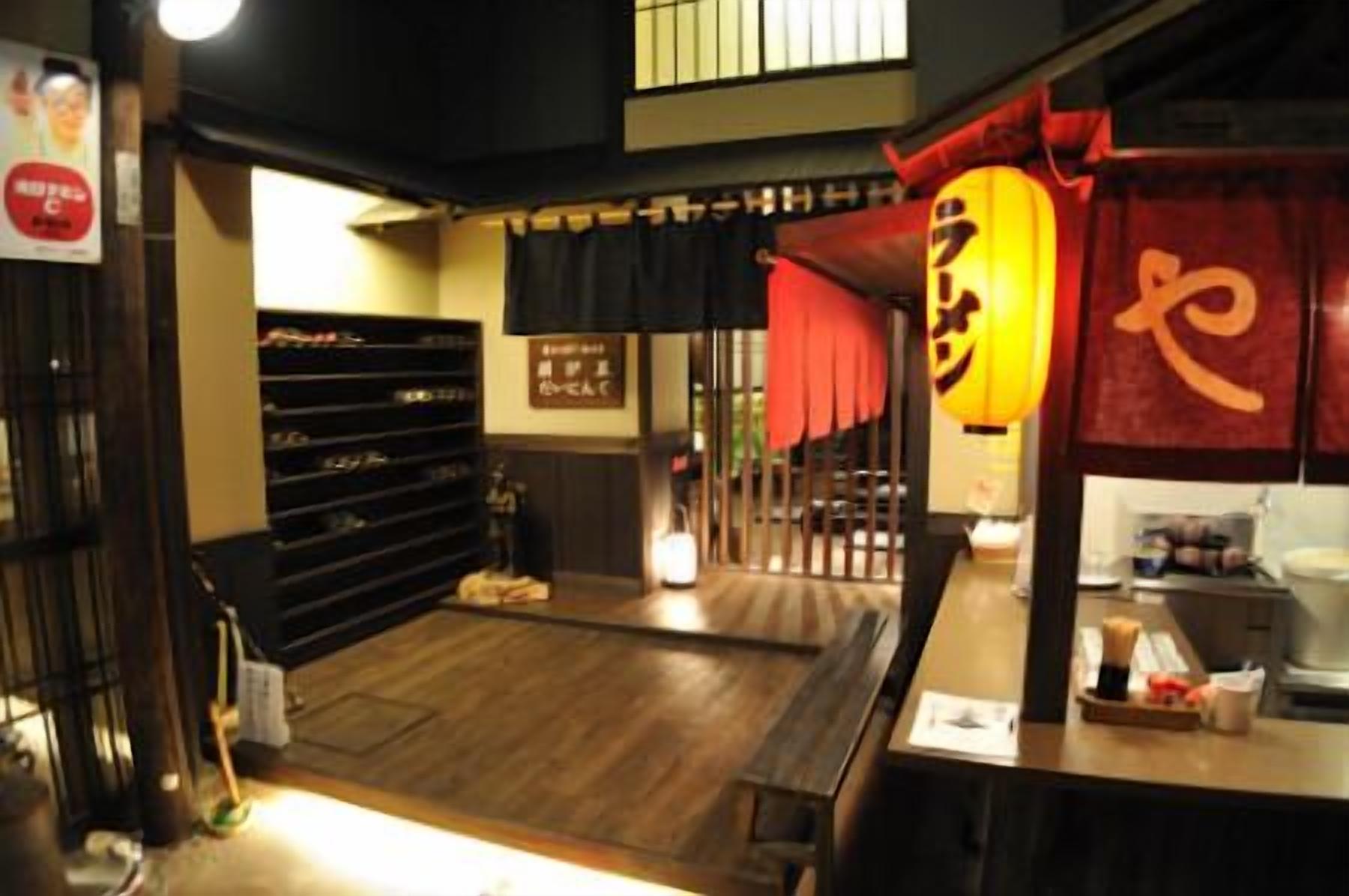 A traditional Japanese restaurant interior with a wooden floor, a counter with a red lantern, and a black shelf with various items.
