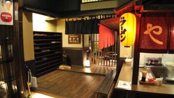 A traditional Japanese restaurant interior with a wooden floor, a counter with a red lantern, and a black shelf with various items.