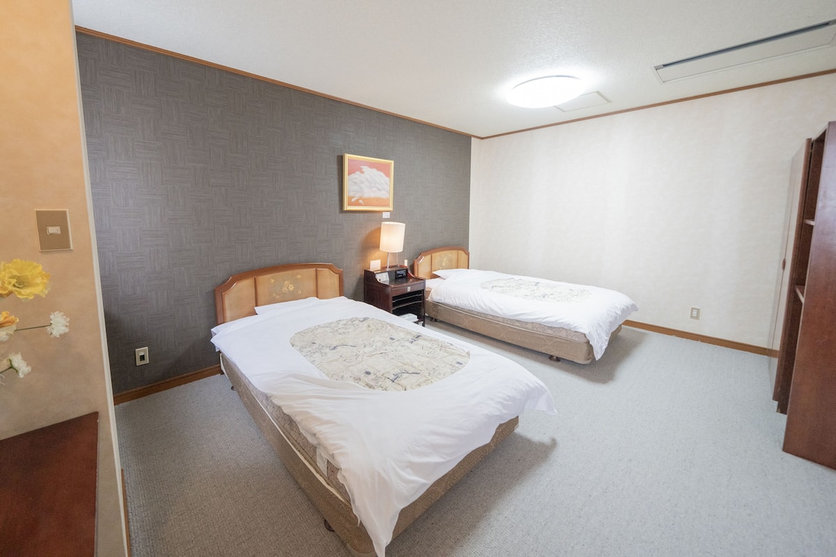 A hotel room with two beds, a nightstand with a lamp, a wall-mounted picture, and a ceiling light.