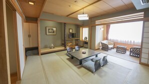A traditional Japanese room with tatami flooring, a low table with cushions, a television, and sliding doors.