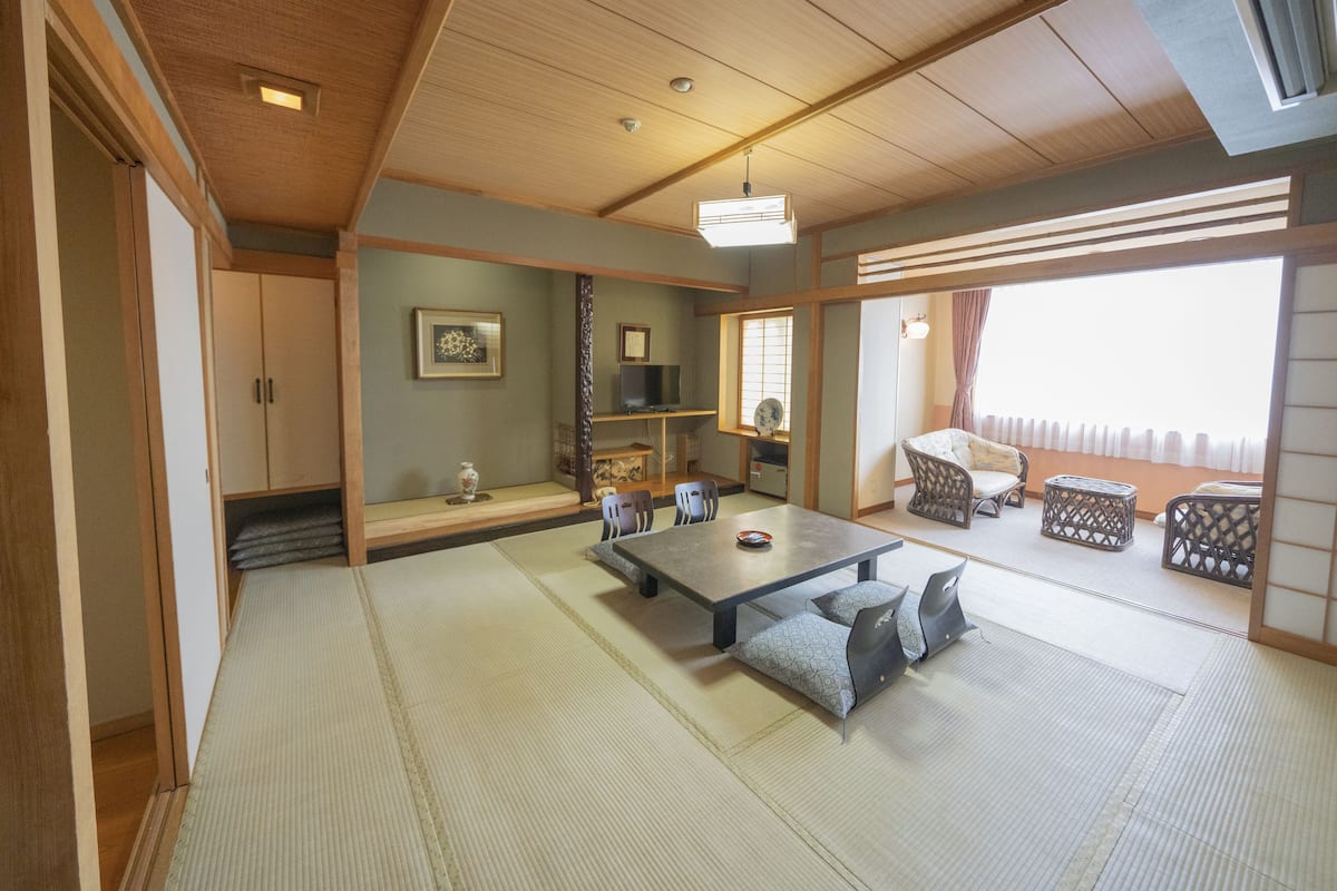 A traditional Japanese room with tatami flooring, a low table with cushions, a television, and sliding doors.