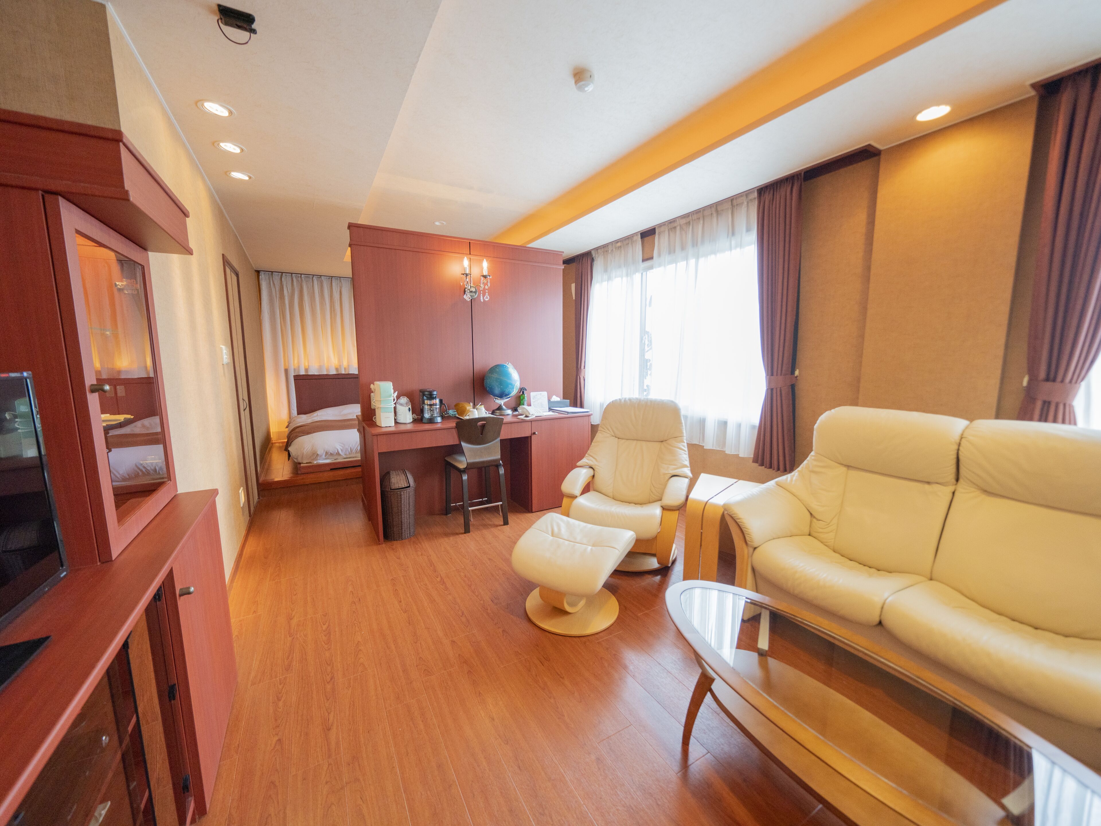 Habitación de hotel con cama, escritorio con globo terráqueo, sillón de cuero, sofá y televisión.
