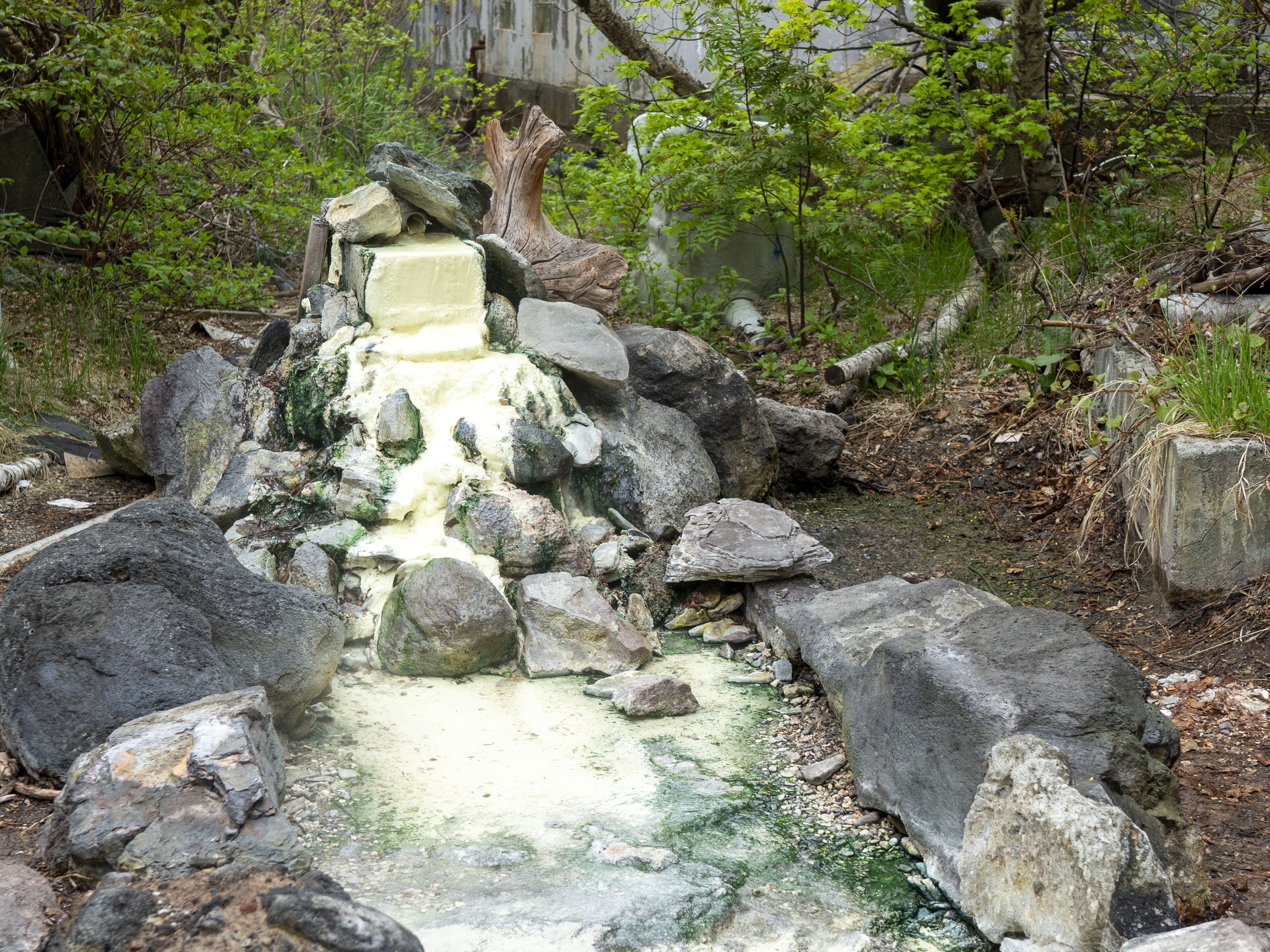 Una formación rocosa natural con una pequeña cascada en una zona boscosa.