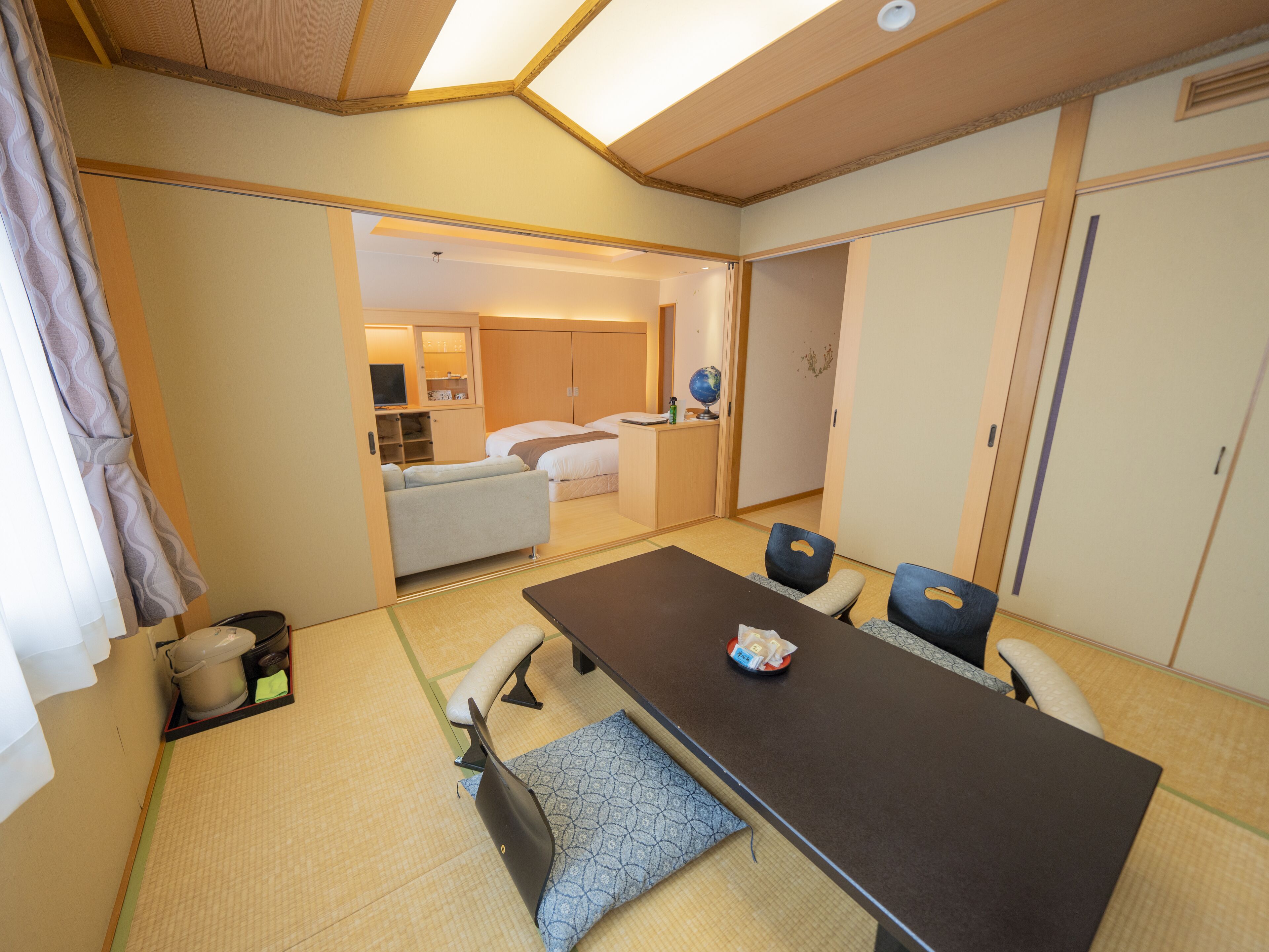 A hotel room with a tatami mat floor, a tatami mat sofa, a small tatami mat table, and a bed with a white headboard.