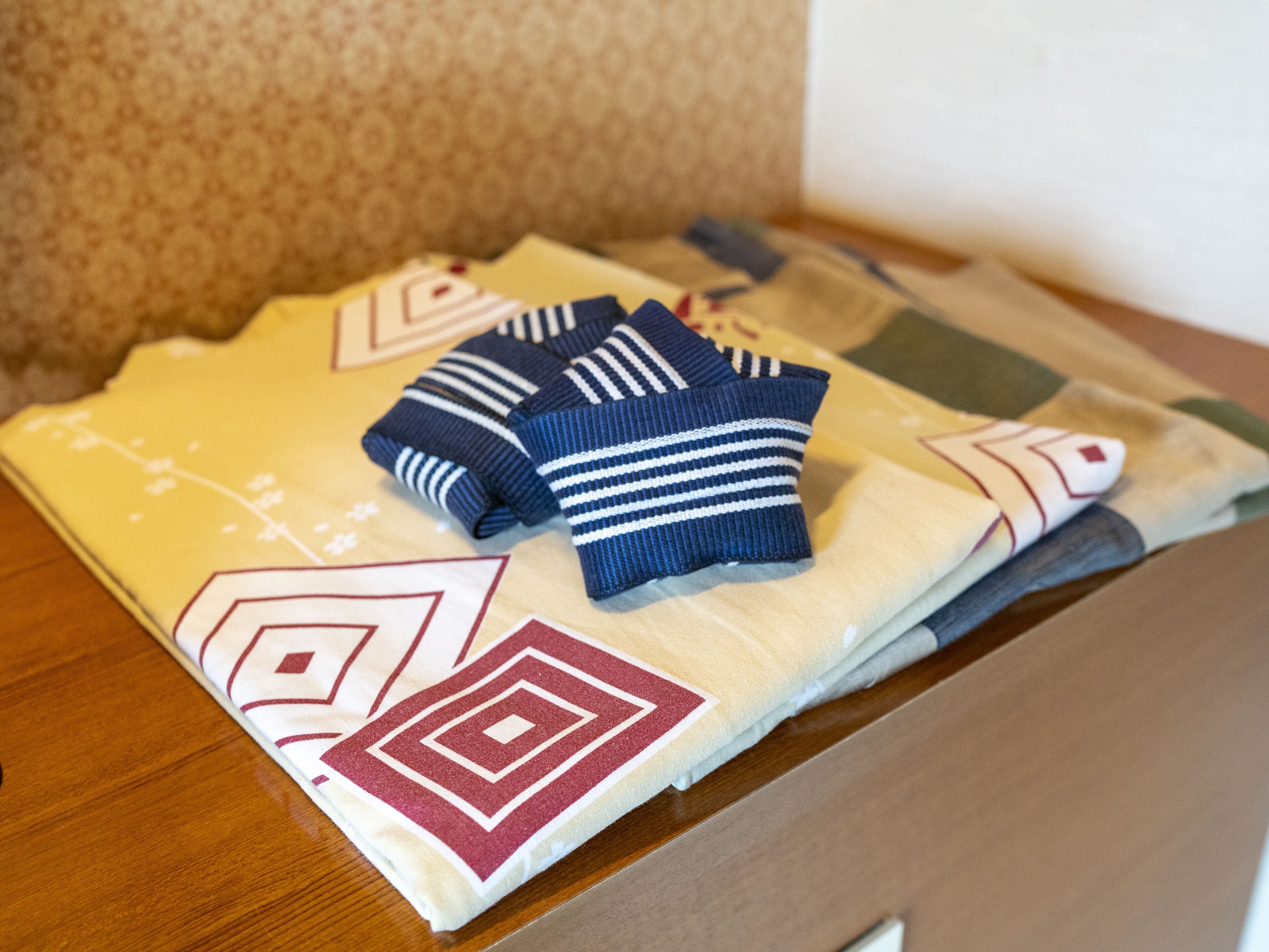 A neatly folded blanket with a geometric pattern and two folded sweaters on a wooden surface.