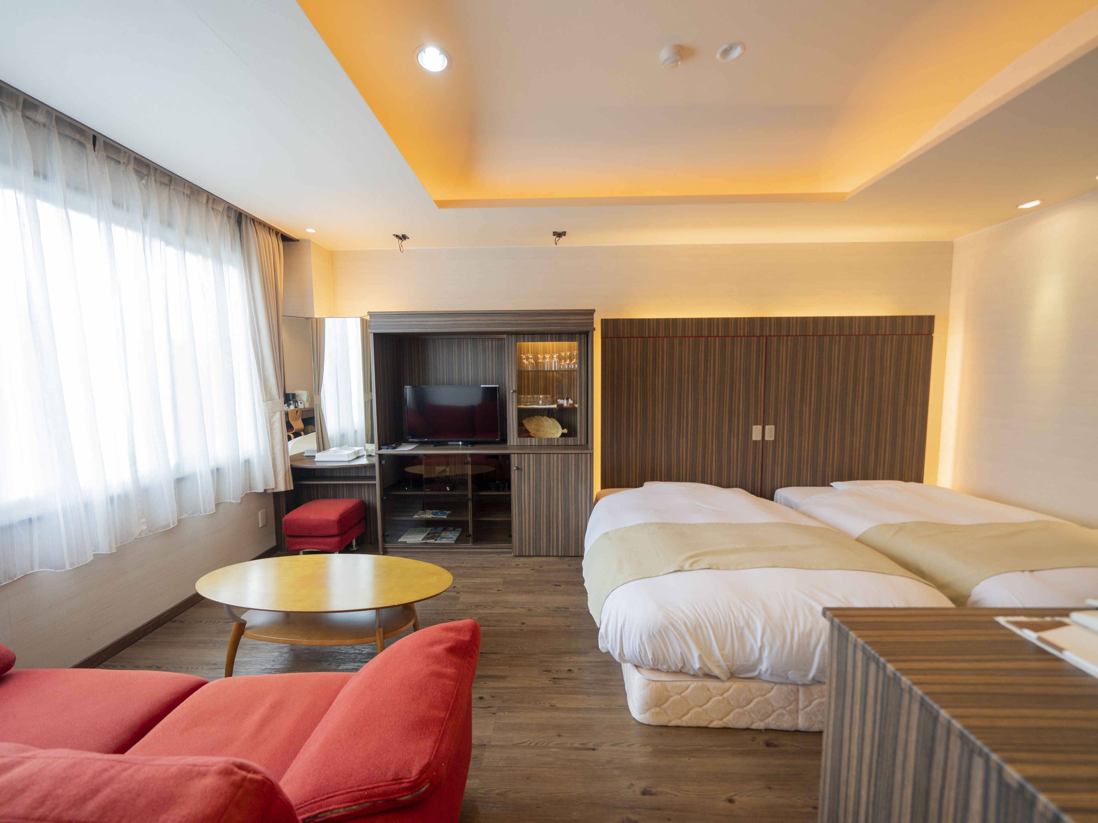 Una habitación de hotel con dos camas, un televisor, una mesita y una silla roja.