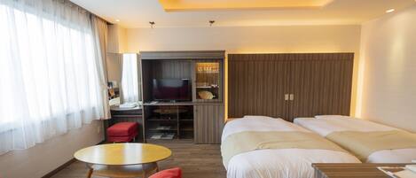 A hotel room with two beds, a TV, a small table, and a red chair.