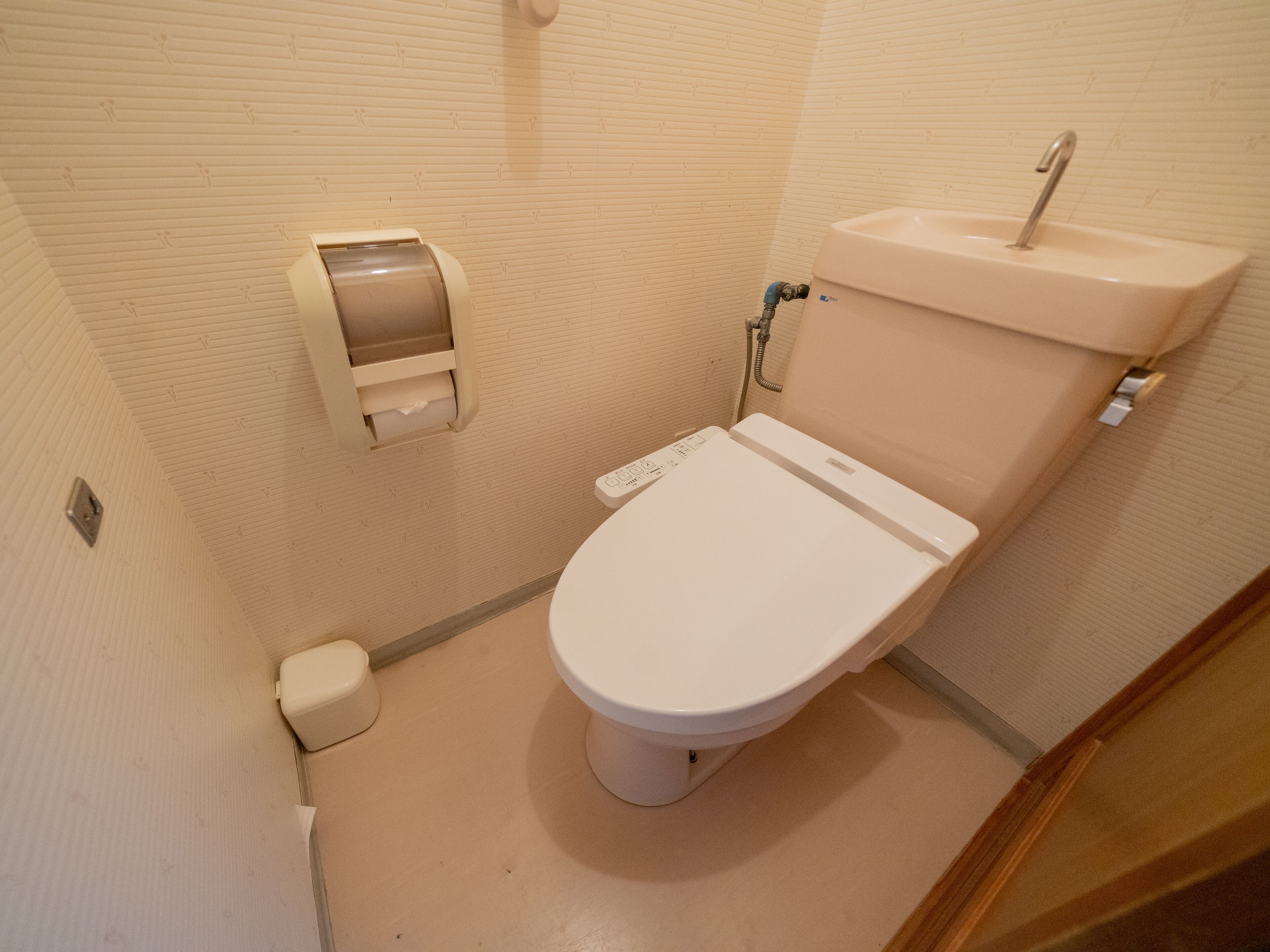 A small, compact bathroom with a toilet, a paper towel dispenser, and a sink.