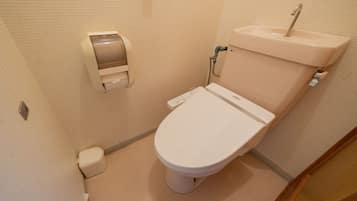 A small, compact bathroom with a toilet, a paper towel dispenser, and a sink.