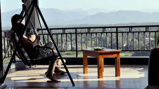 A balcony with a swing chair, a small wooden table, and a view of distant mountains. - Villa Tranquil (Kandy)
