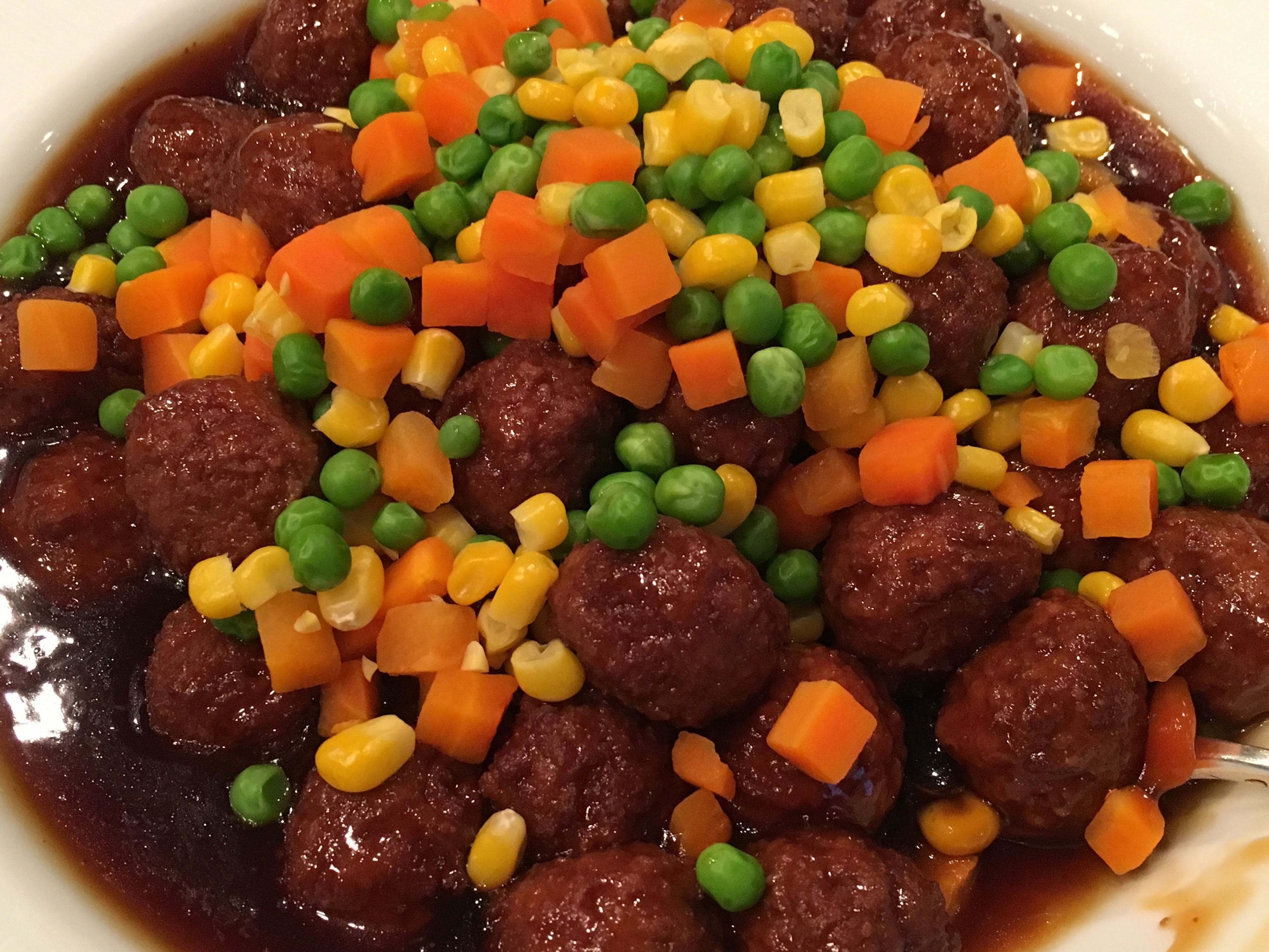 A bowl of meatballs with peas, carrots, and corn.