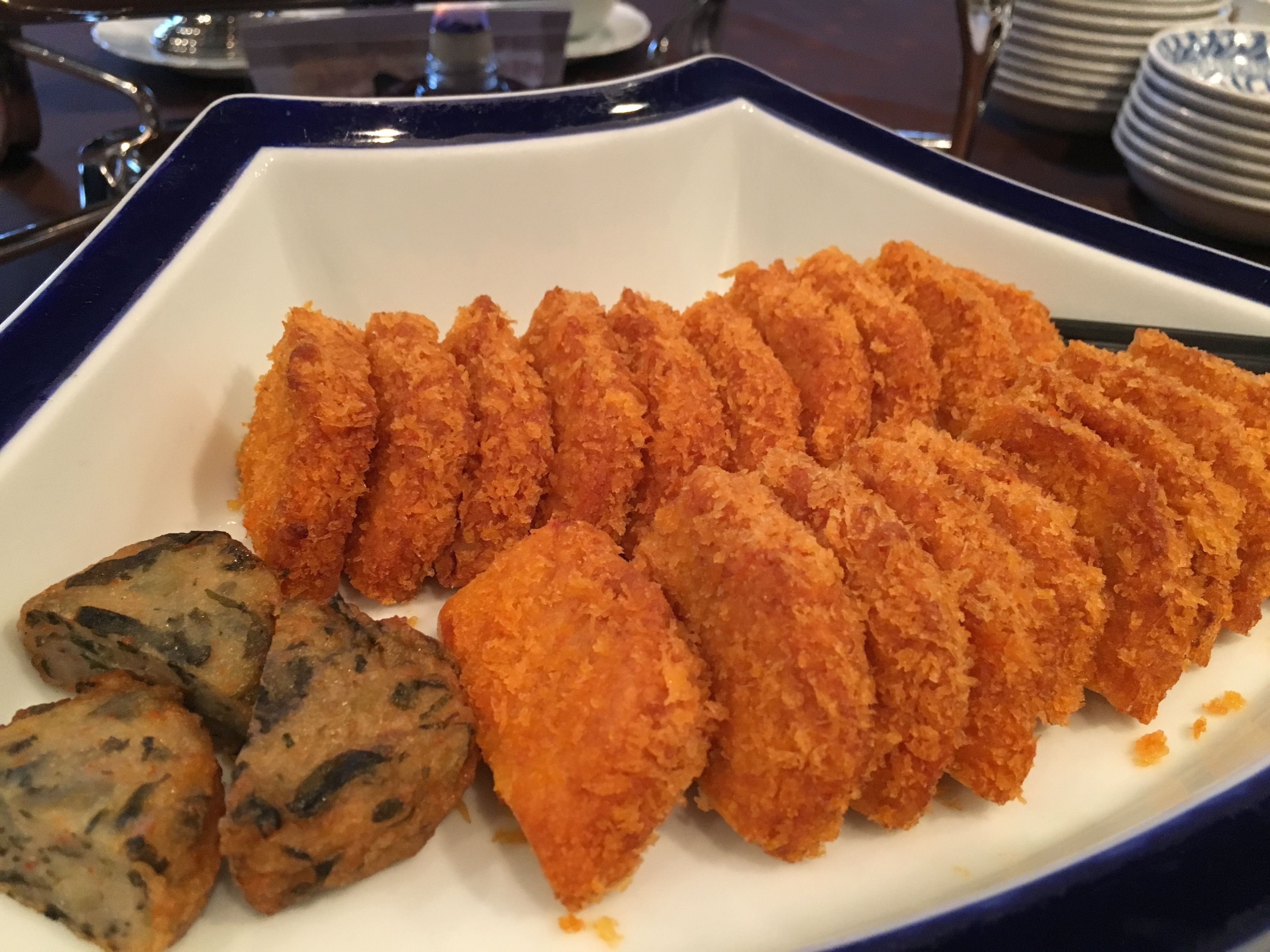 Une assiette de mets panés et frits, peut-être des croquettes, servis sur une assiette blanche à bordure bleue.