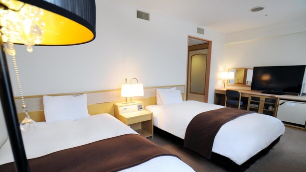 Ein Hotelzimmer mit zwei Betten, einem Schreibtisch, einem Fernseher und einer Lampe.