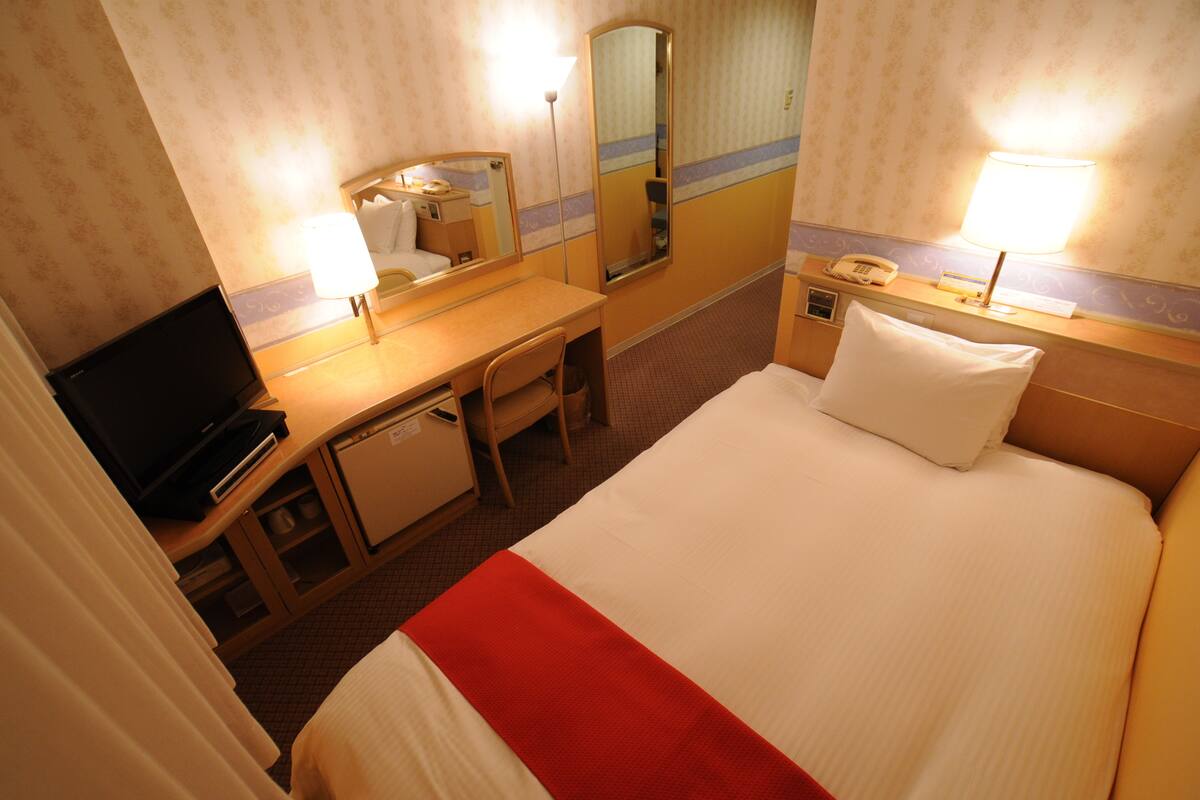 Une chambre d’hôtel comprenant un lit, un bureau, une chaise, une télévision et un miroir.