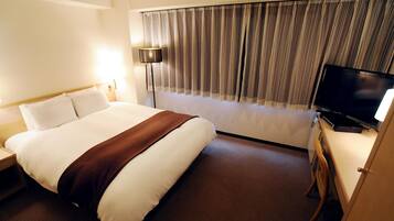 A hotel room with a large bed, a flat-screen TV, a desk with a chair, and a window with curtains.