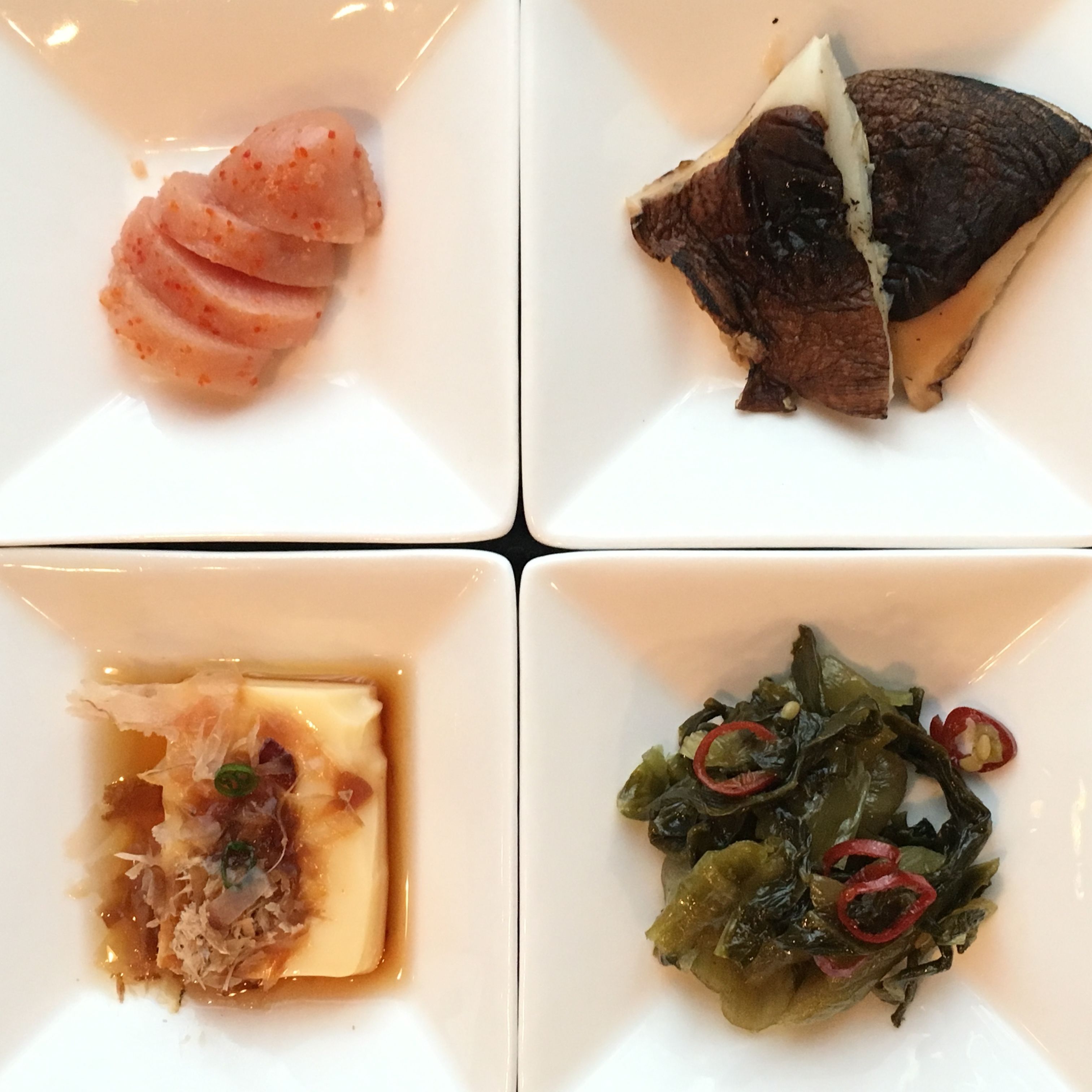 Un plat quadrat amb quatre plats diferents: una porció de carn, un tros de peix, un bol de sopa i un plat de verdures.