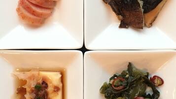 Un plat quadrat amb quatre plats diferents: una porció de carn, un tros de peix, un bol de sopa i un plat de verdures.