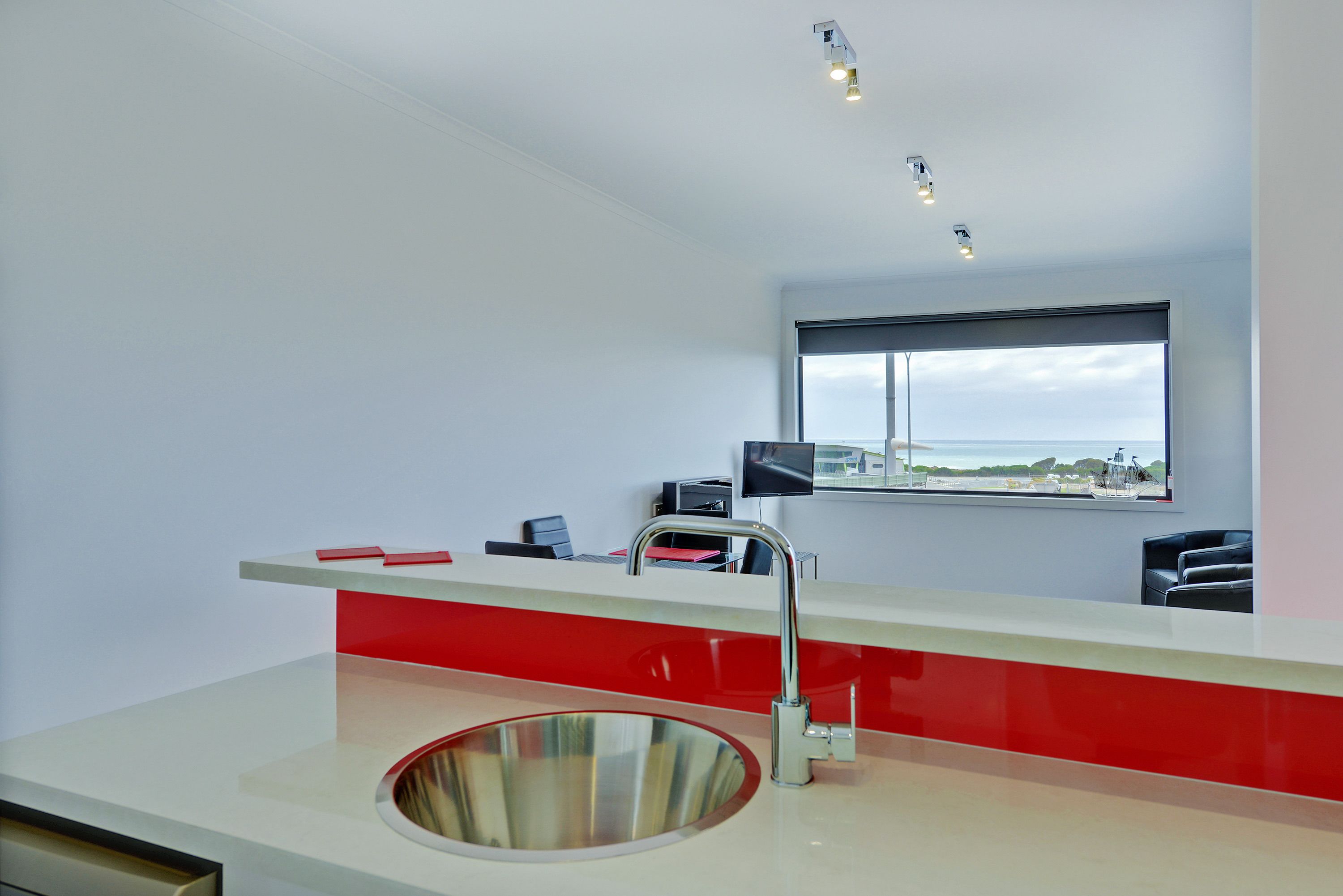 Una cocina moderna con un lavamanos de acero inoxidable, una encimera roja y blanca, y un ventanal con vistas panorámicas.