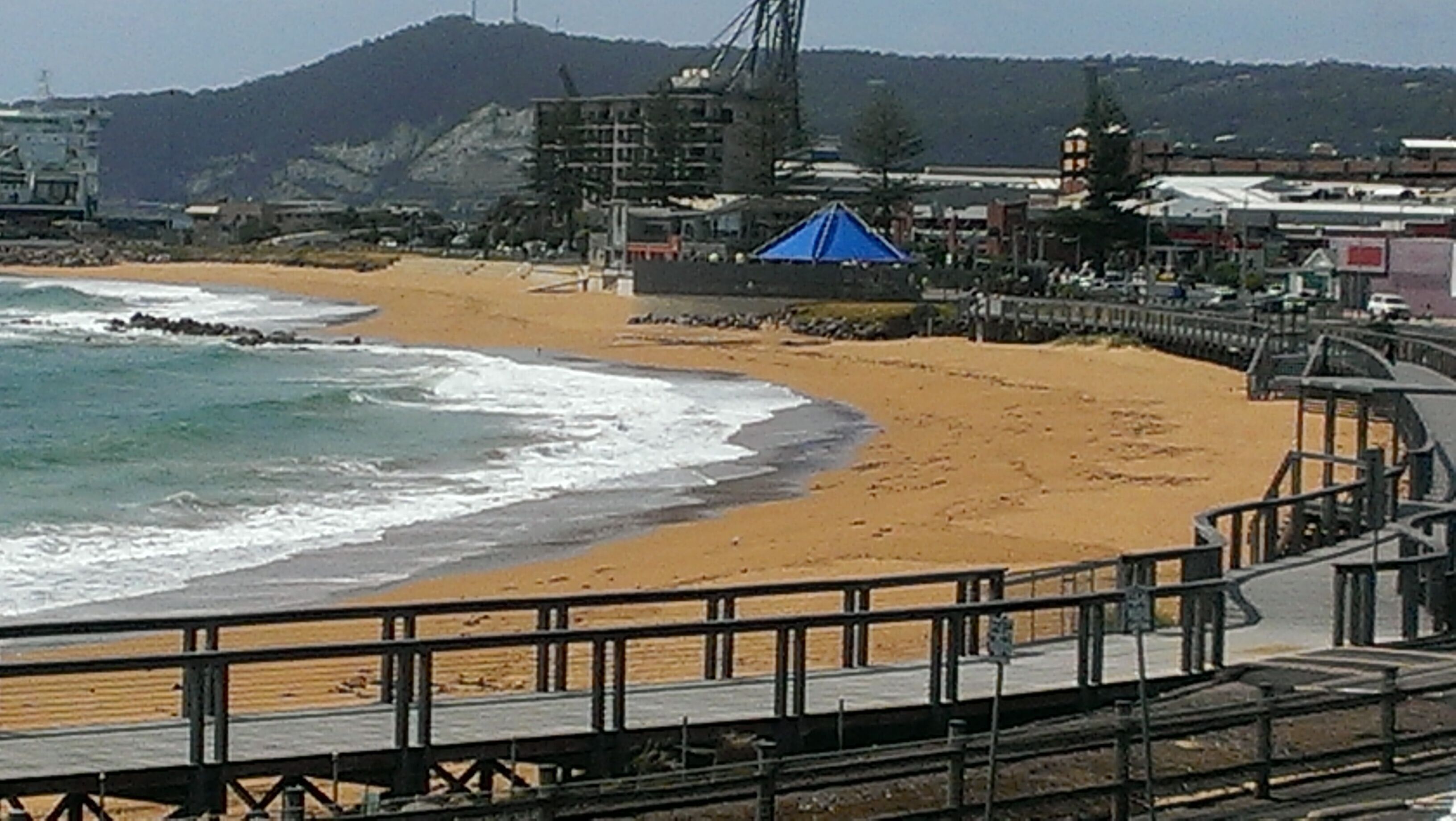 Une plage avec une promenade en bois, une tente bleue et des bâtiments en arrière-plan.