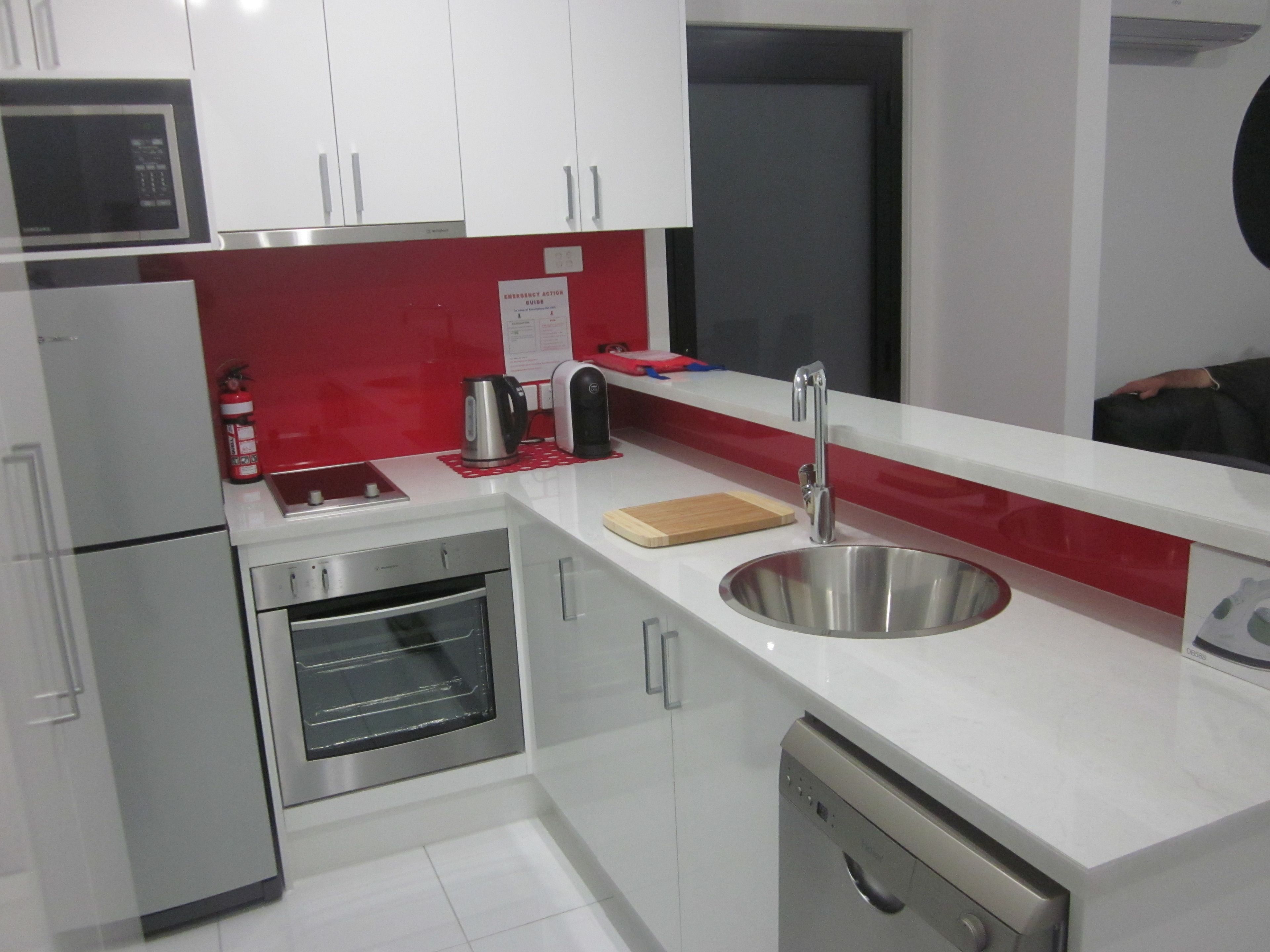 A modern kitchen with stainless steel appliances, a red backsplash, and a built-in dishwasher.