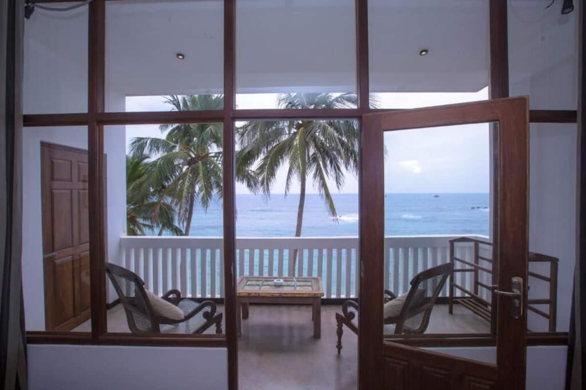 Una habitación con vista al océano y palmeras, que incluye una mesa de madera y dos sillas de mimbre.