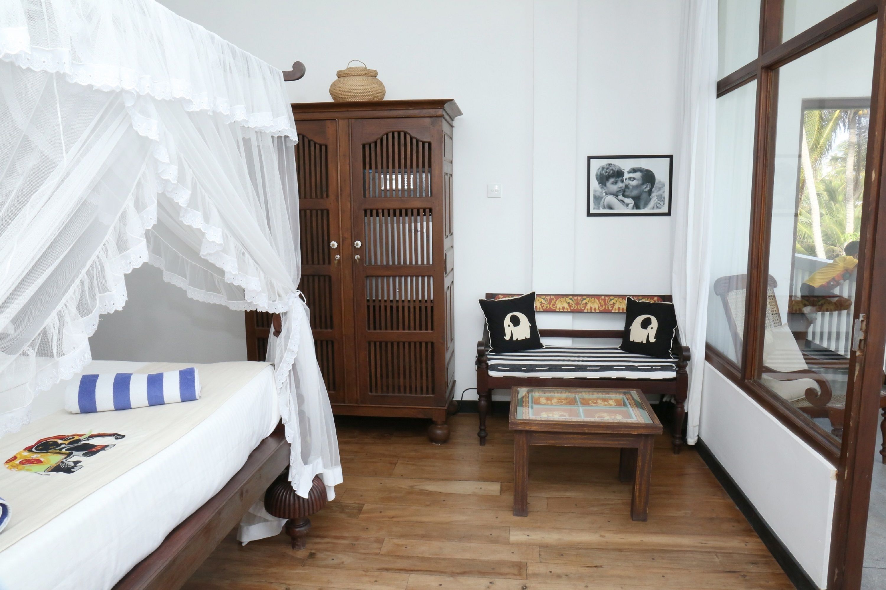 A bedroom with a bed under a canopy, a wooden cabinet, a bench with decorative pillows, and a framed picture on the wall.