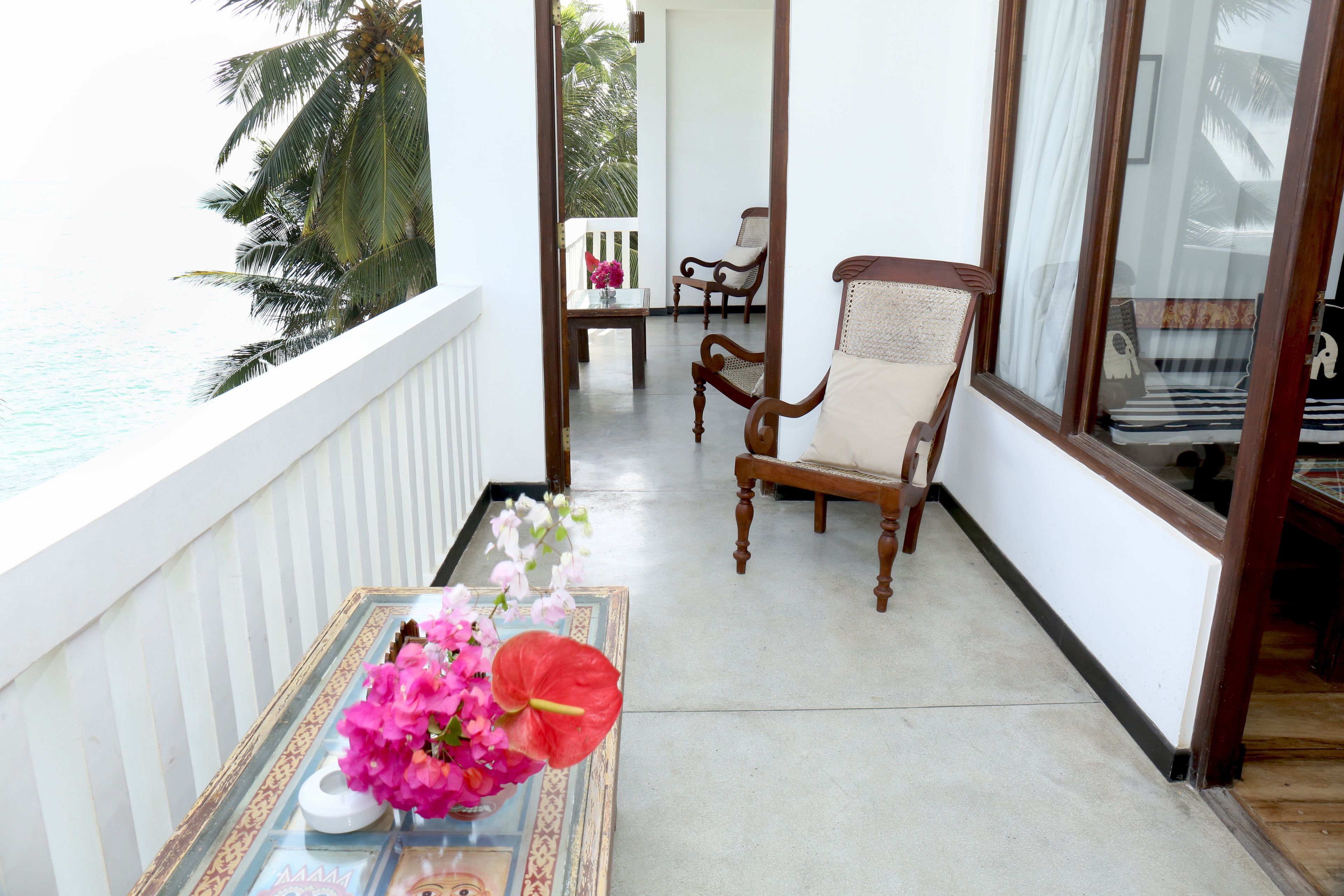 Ein Balkon mit Tisch, auf dem Blumen stehen, ein Stuhl und Blick aufs Meer.