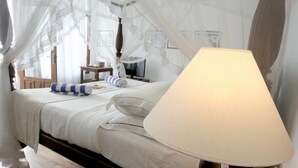 Quarto com cama de dossel, mesa de cabeceira com abajur e criado-mudo pequeno.