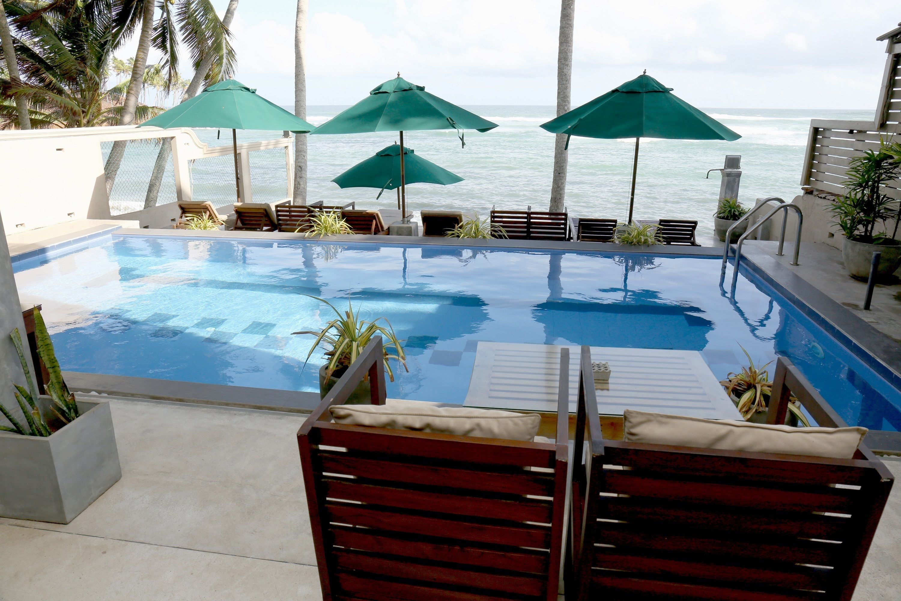 An infinity pool with a view of the ocean, surrounded by lounge chairs and green umbrellas.