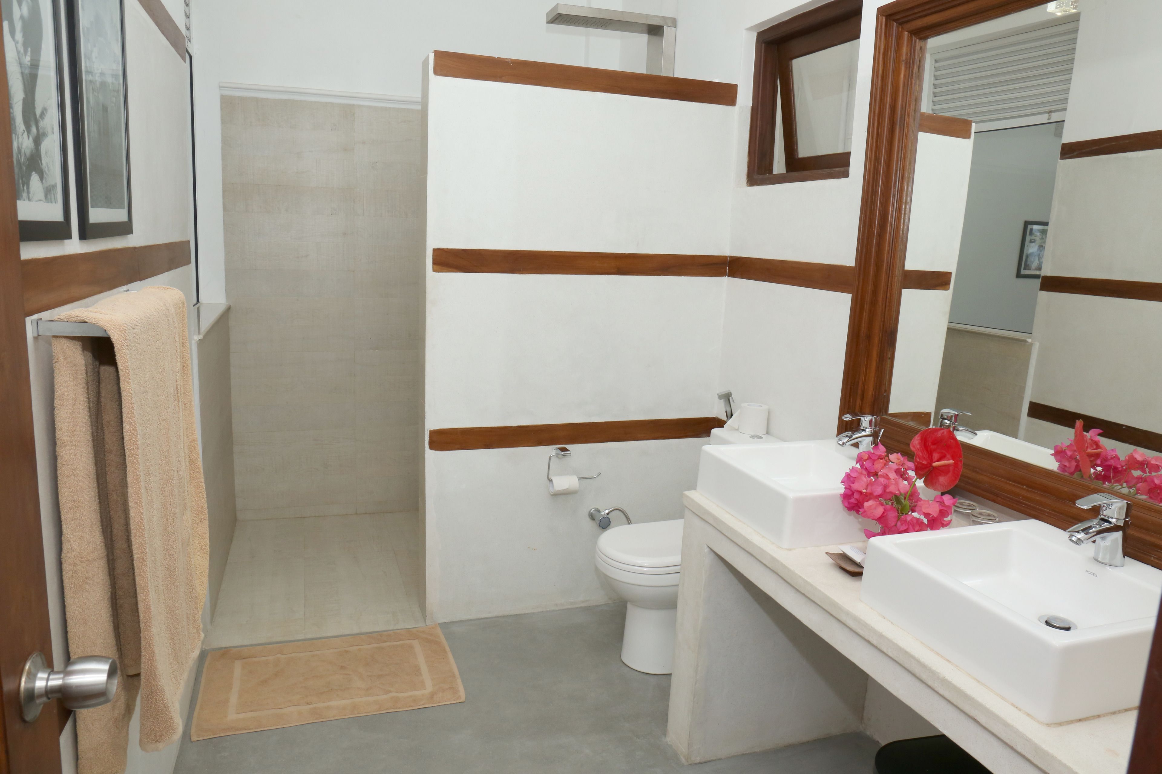 A bathroom with a toilet, two sinks, a mirror, and a shower.